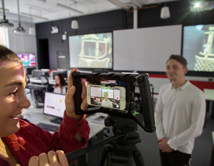 Student filming in the newsroom on a smartphone.