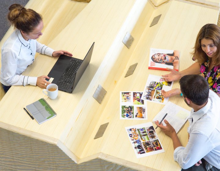 Two women and a man seated at a desk with a laptop and print outs