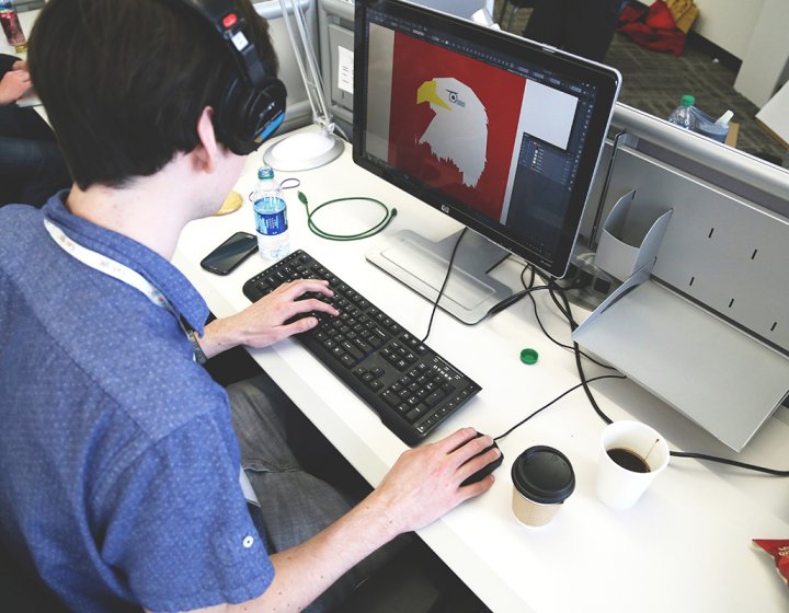 Student with headphones on working on InDesign at a desktop.