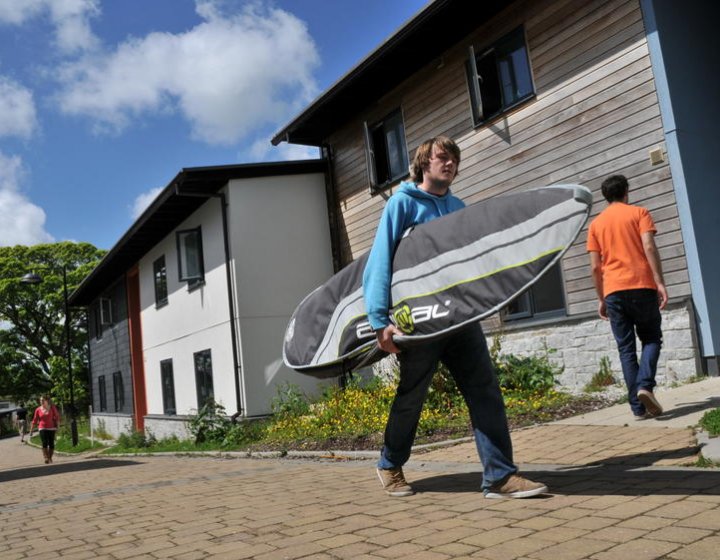 Student carrying surfboard outside student accommodation.