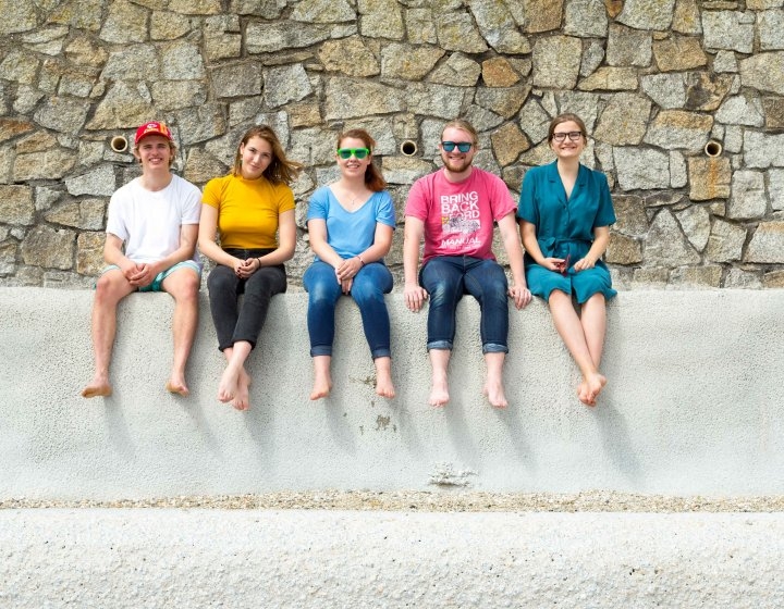 Barefooted students sitting on a wall at the beach.