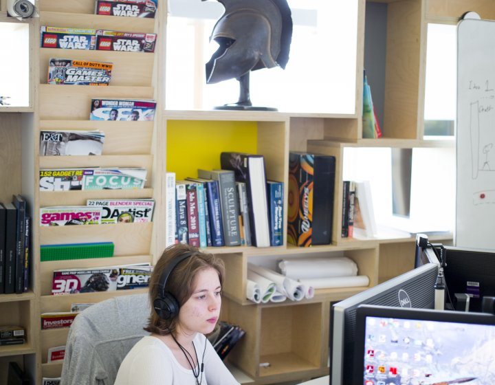 Female student wearing headphones and a white sweater at a computer