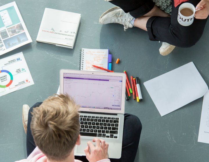 Two Falmouth University students sitting on the floor with a laptop and pieces of paper