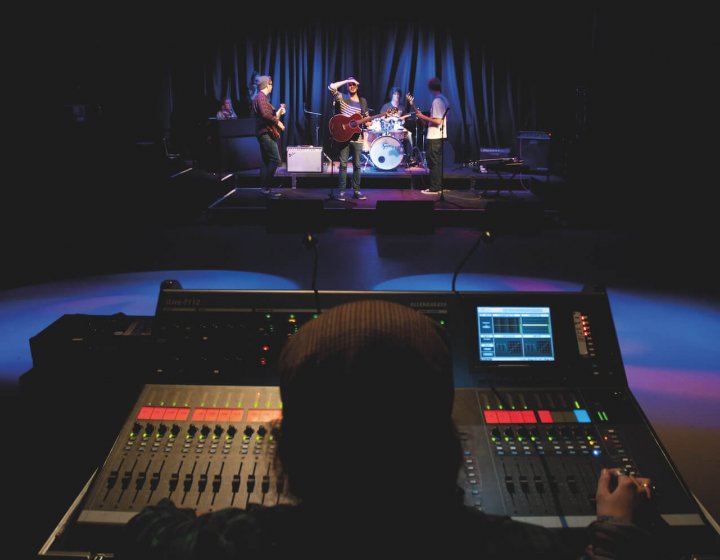 A student behind a sound desk with a view of a band performing
