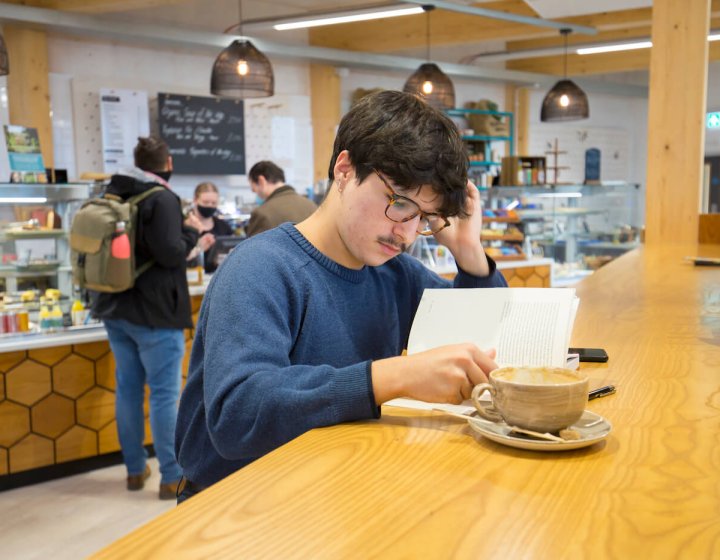 A student reading at a table in the cafe on Penryn Campus