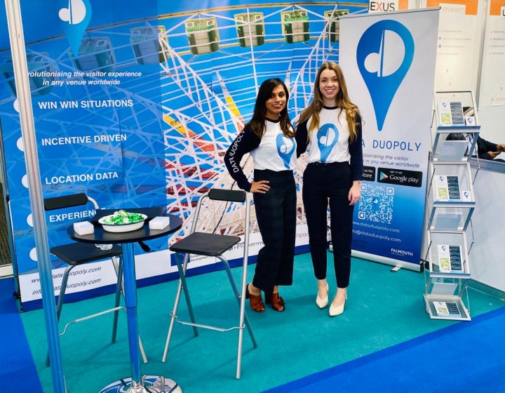 Two women standing together in a blue Data Duopoly exhibition stand