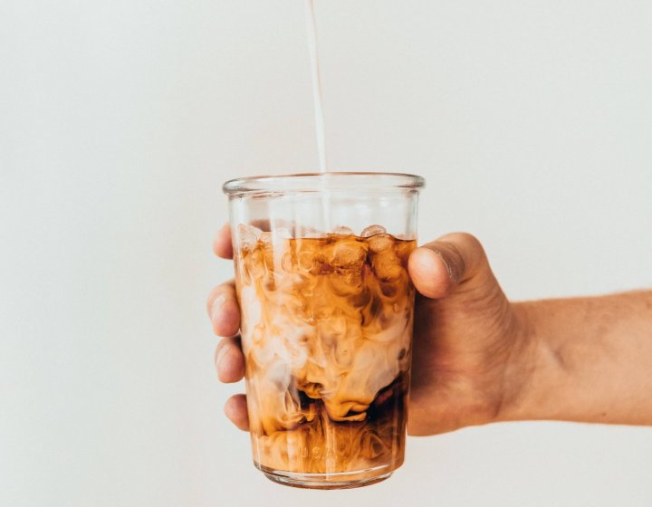 Photo of hand holding out a glass of iced coffee. Photo by Tavis Beck.