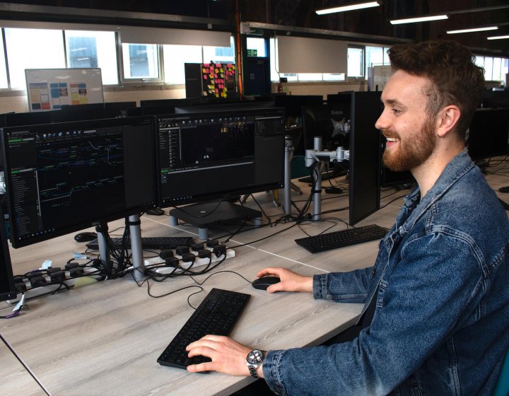 A Falmouth University Games student smiling at a computer screen with a keyboard and mouse