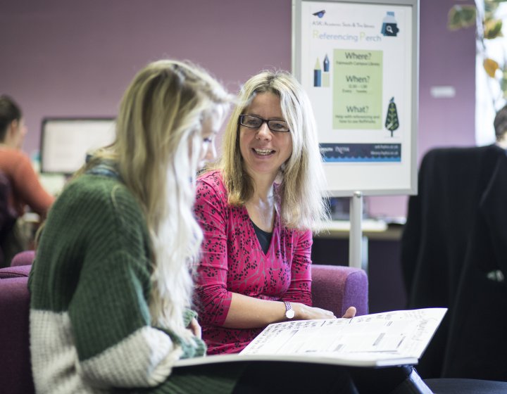 Member of staff chatting with student in library.