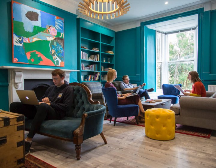 Falmouth University students sitting on armchairs and sofas in a teal room with wooden floor