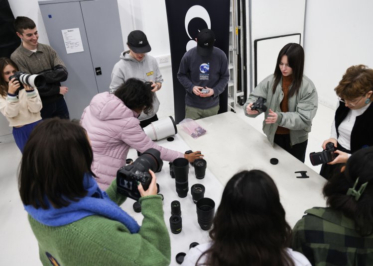 A group of students stood around a white table looking at camera equipment