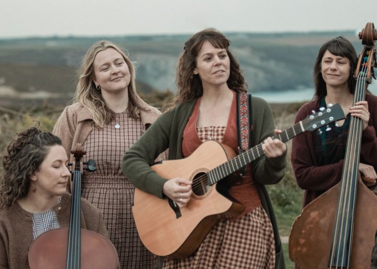 4 musicians holding instruments set against the rugged Cornish cliffs