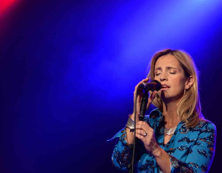 A person stood on stage under lighting singing into a handheld microphone