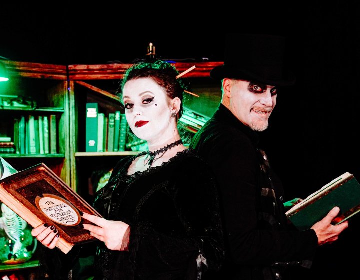 Two performers dressed in gothic costumes holding books and looking at the camera