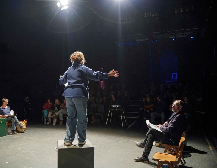 Performer with their back to the camera on stage under a spotlight performing to an audience