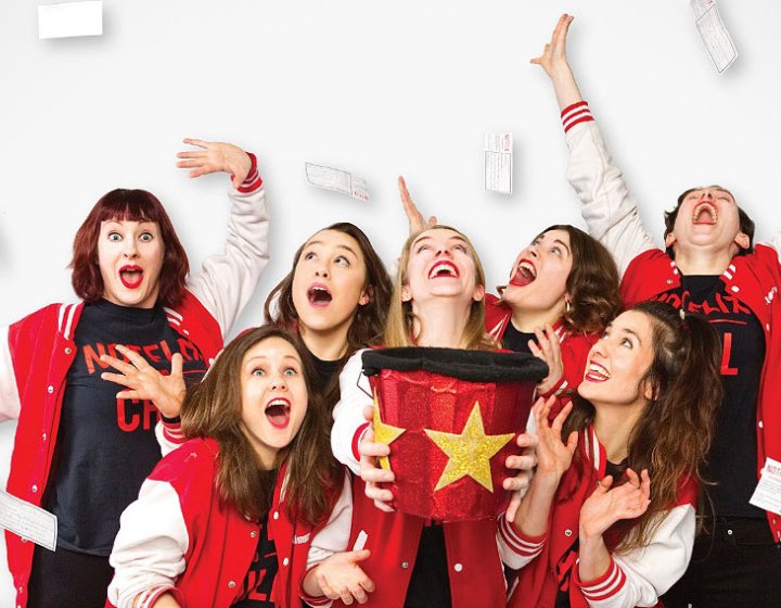 A group of performers posing in red outfits on a white background on top of the Notflix logo
