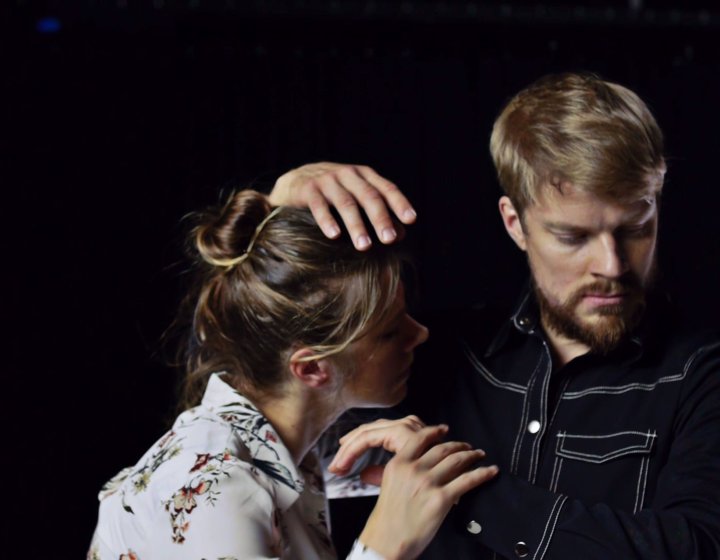 Two performers dancing on in close contact against a dark black backdrop
