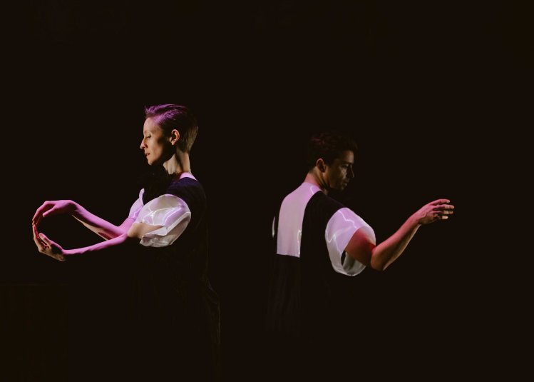 Two dancers wearing black and white costumes dancing against a black background