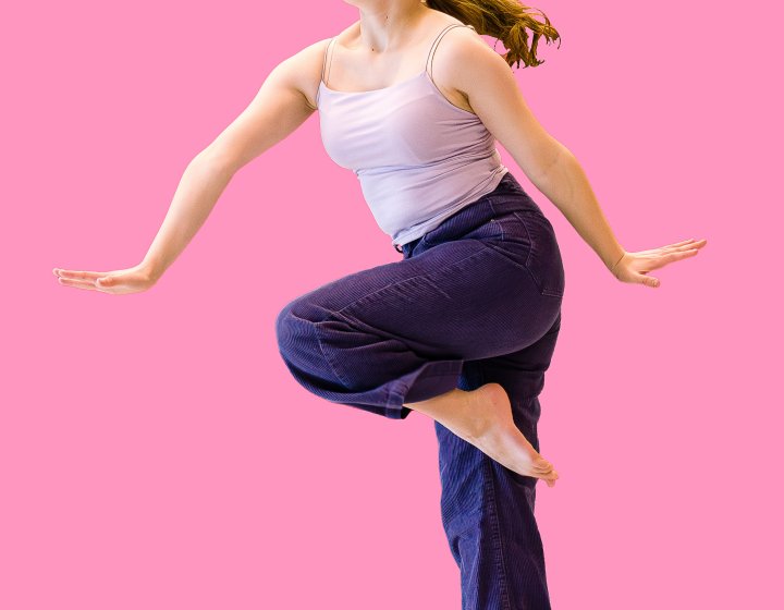 An image of a young female dancer jumping in the air against a bright pink backdrop