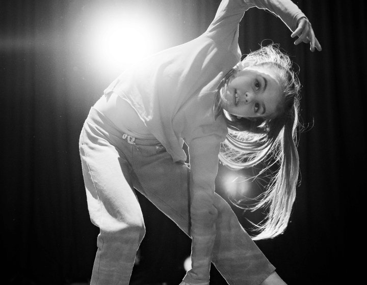 A black and white image of a young dance posing for the camera with a bright light in the background