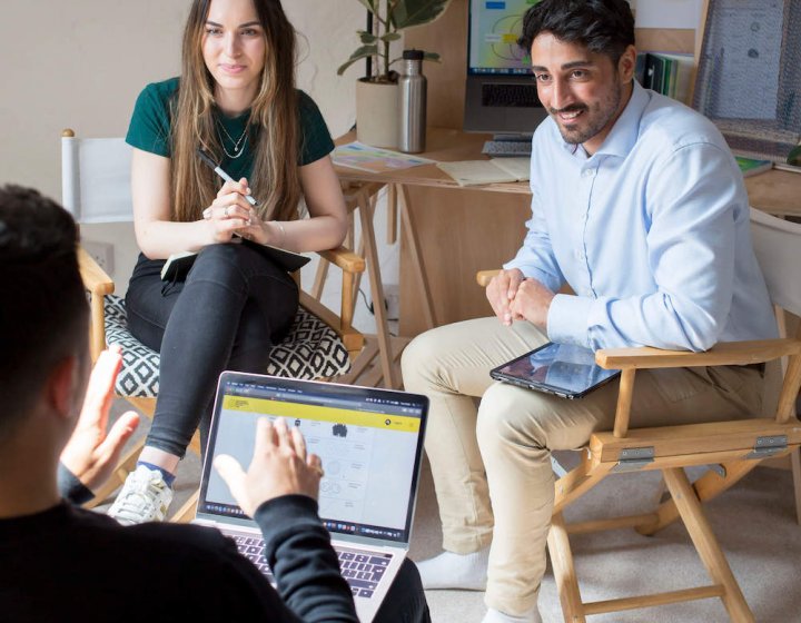 Three people seated in conversation with graphs and a plant in the background