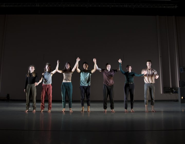 A line of dance students holding hands on a stage