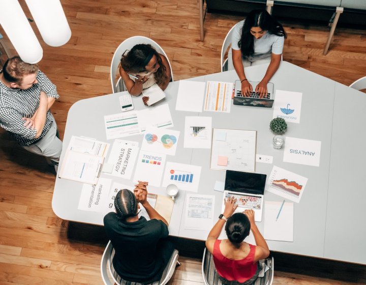 Birds eye view of group of people sat around a table with business strategy papers