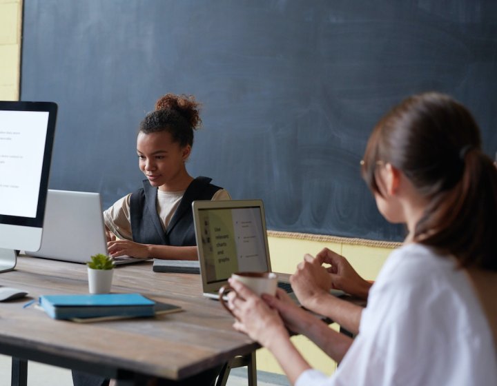 Three people studying at laptops on a table with a notebook and plant