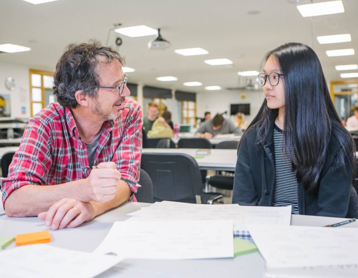 a male staff member talking to a female student at a desk