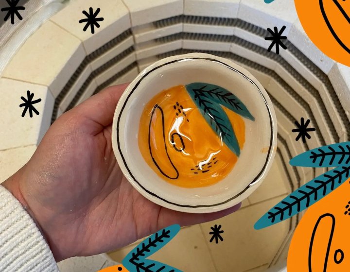A hand holding a ceramic bowl painted as an orange