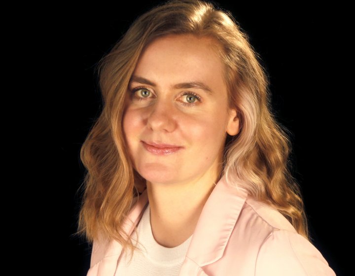 A portrait image of a woman, wearing a pink jacket and a patterned jumper