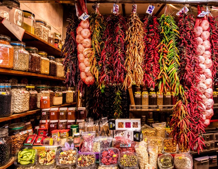 Spices and garlic hang from a market stall, with jars of dried goods surrounding the stall