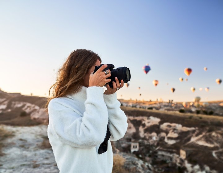 A student taking a photo standing underneath a sky full of hot air balloons