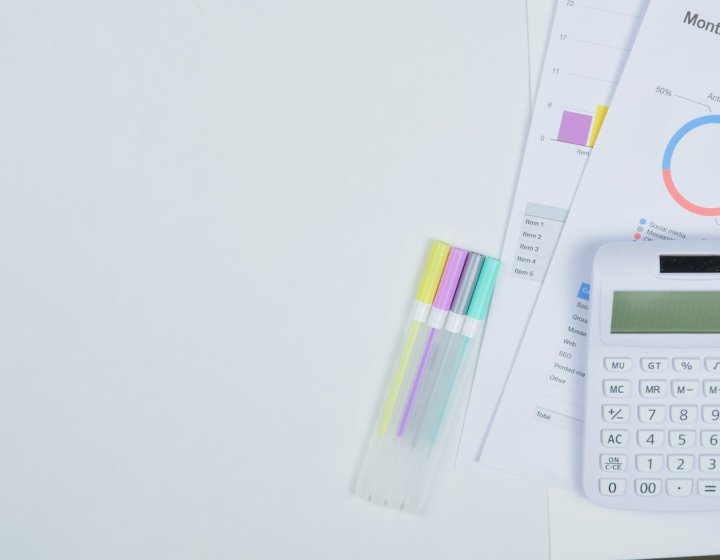 A white calculator and pens next to paper with financial graphs