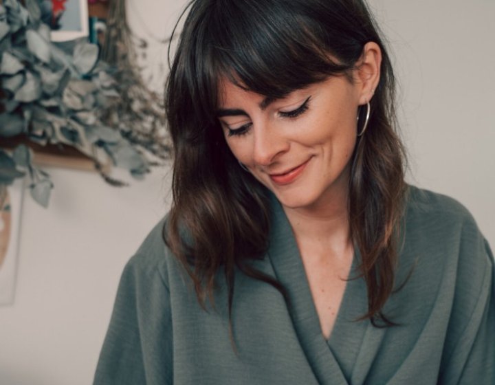 A woman with dark hair looking down and wearing an olive green top