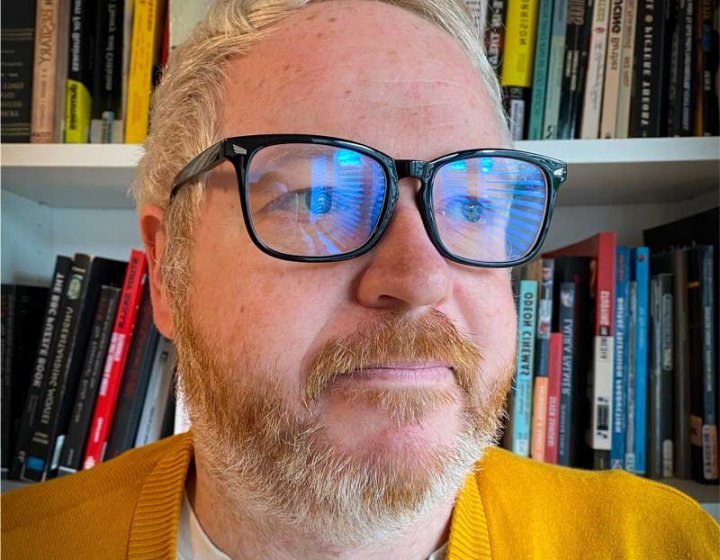 A headshot of Film & TV student Rich Scott smiling wearing glasses and a yellow jumper