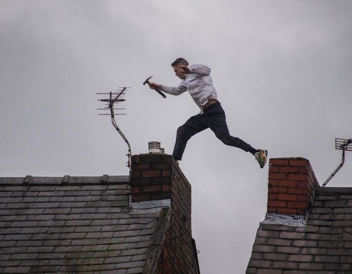 Photo of a man holding a hammer jumping from one rooftop to another during a protest in Manchester.