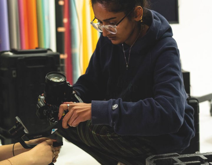 A girl wearing glasses crouched down holding a camera