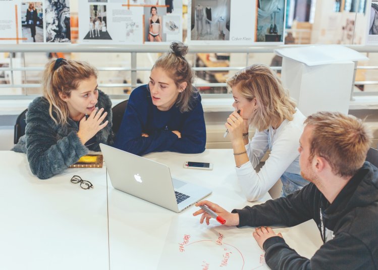 Group of Fashion Marketing students sat talking in front of laptop at Falmouth University