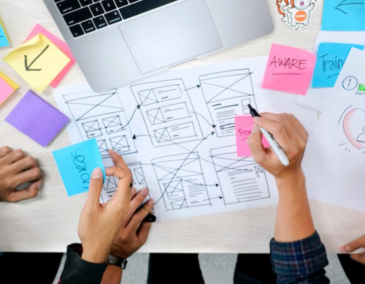 hands sketching a sitemap with a laptop and coloured post-it notes on a table