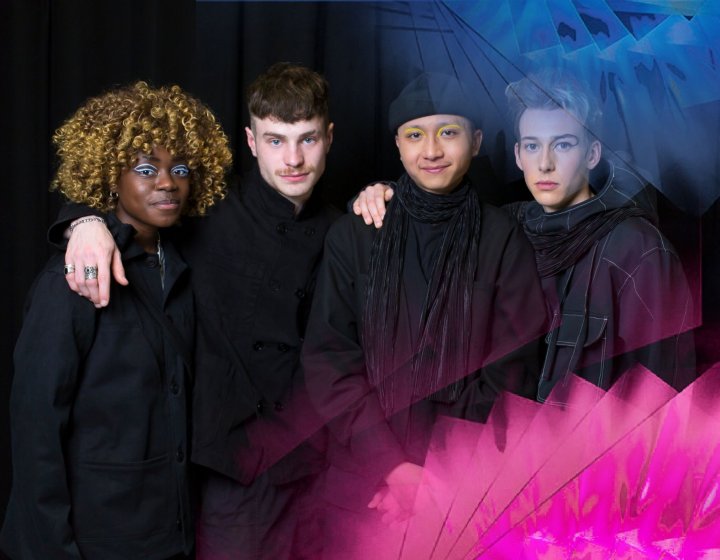 Four students standing together and looking into the camera wearing black garments designs by a student.