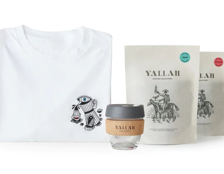 White t-shirt with black illustration, glass coffee cup with cork cover and black lid, and two bags of Yallah coffee. 
