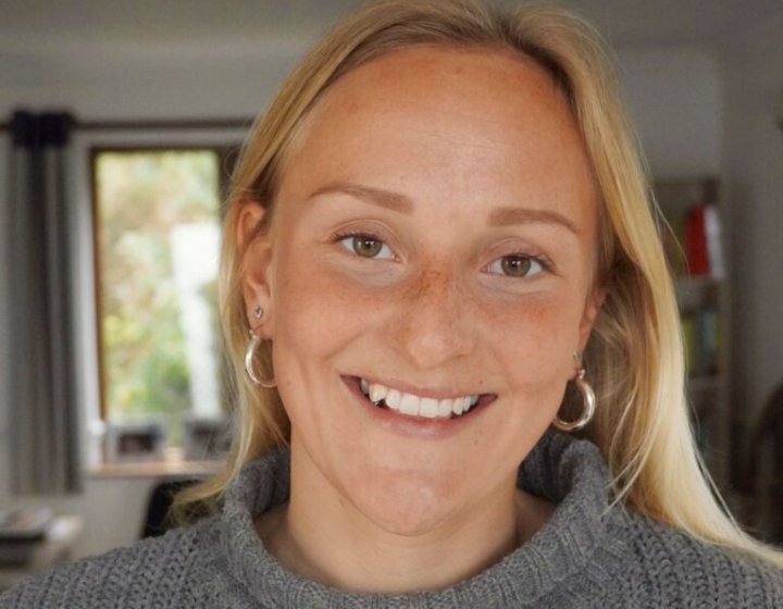 A blonde haired woman wearing a grey jumper smiles 