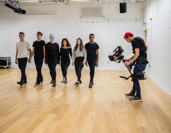6 people walking in a line in a studio filmed by a lone cameraman