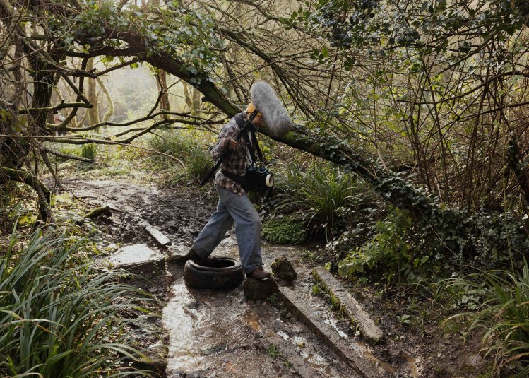 A person walking in a woodland with a large microphone