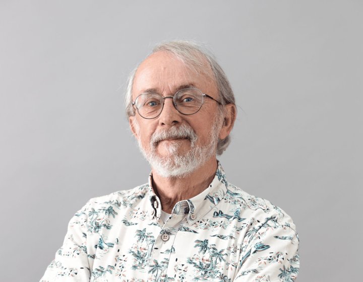 Headshot of Peter Lord against a grey background with a flowery shirt and glasses and a beard