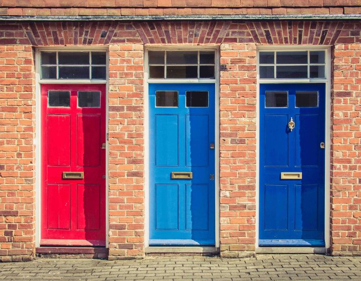 A row of 3 colourful front doors on a brick building