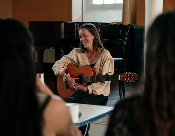 A musician sat in front od a piano playing an acoustic guitar