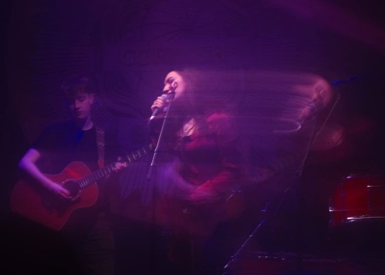 A photo of people performing which is slightly blurred with pink and purple lighting