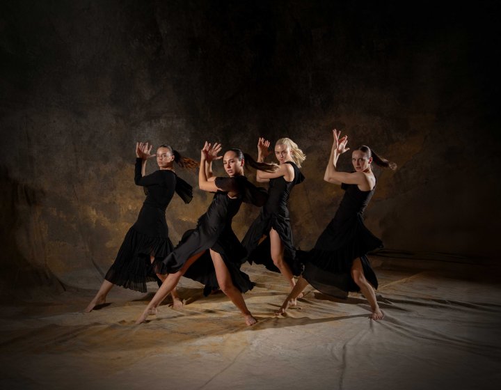 4 female dancers posing on a staged background wearing all black